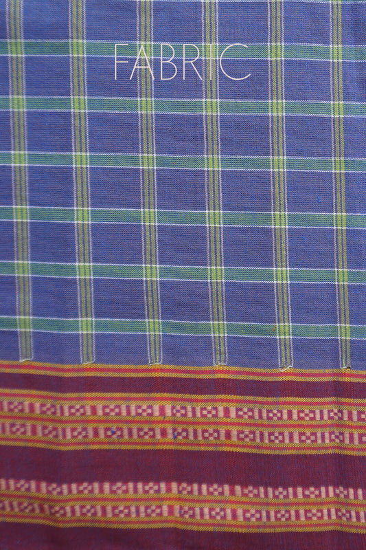 A close-up of a woven Kunbi fabric with a blue base, green and yellow vertical stripes, and a decorative multicolor patterned border at the bottom. The word 'FABRIC' is printed across the top.