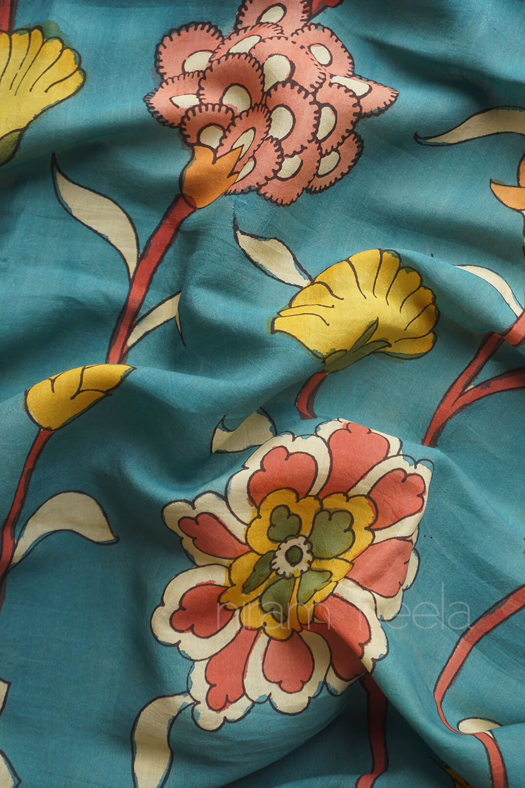 A close-up of a teal blue fabric with a hand-painted floral pattern in pink, yellow, and white.