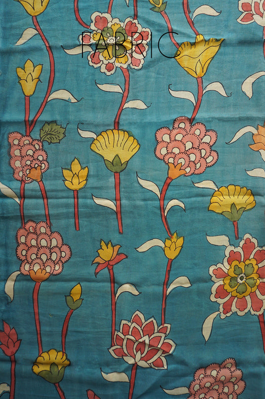 A close-up of a fabric with a hand-painted floral pattern on a teal blue background. The design features pink, yellow, and red flowers with white and green leaves.
