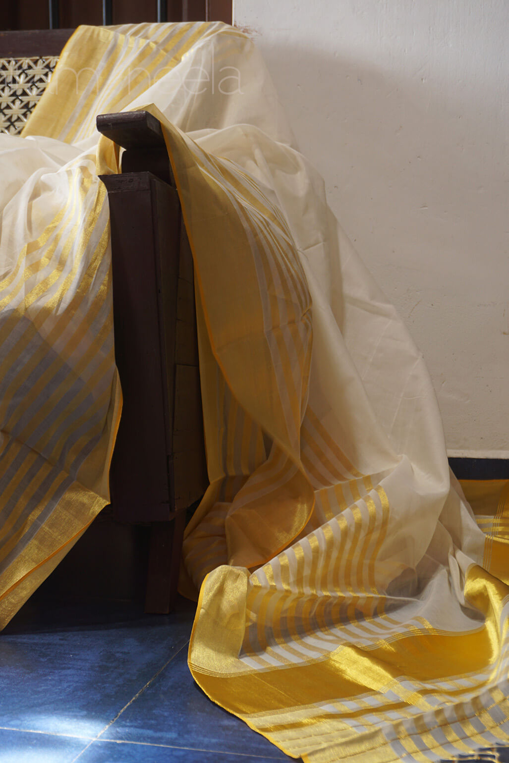 Golden and white striped fabric draped over a bed with a blue floor | Niram Neela