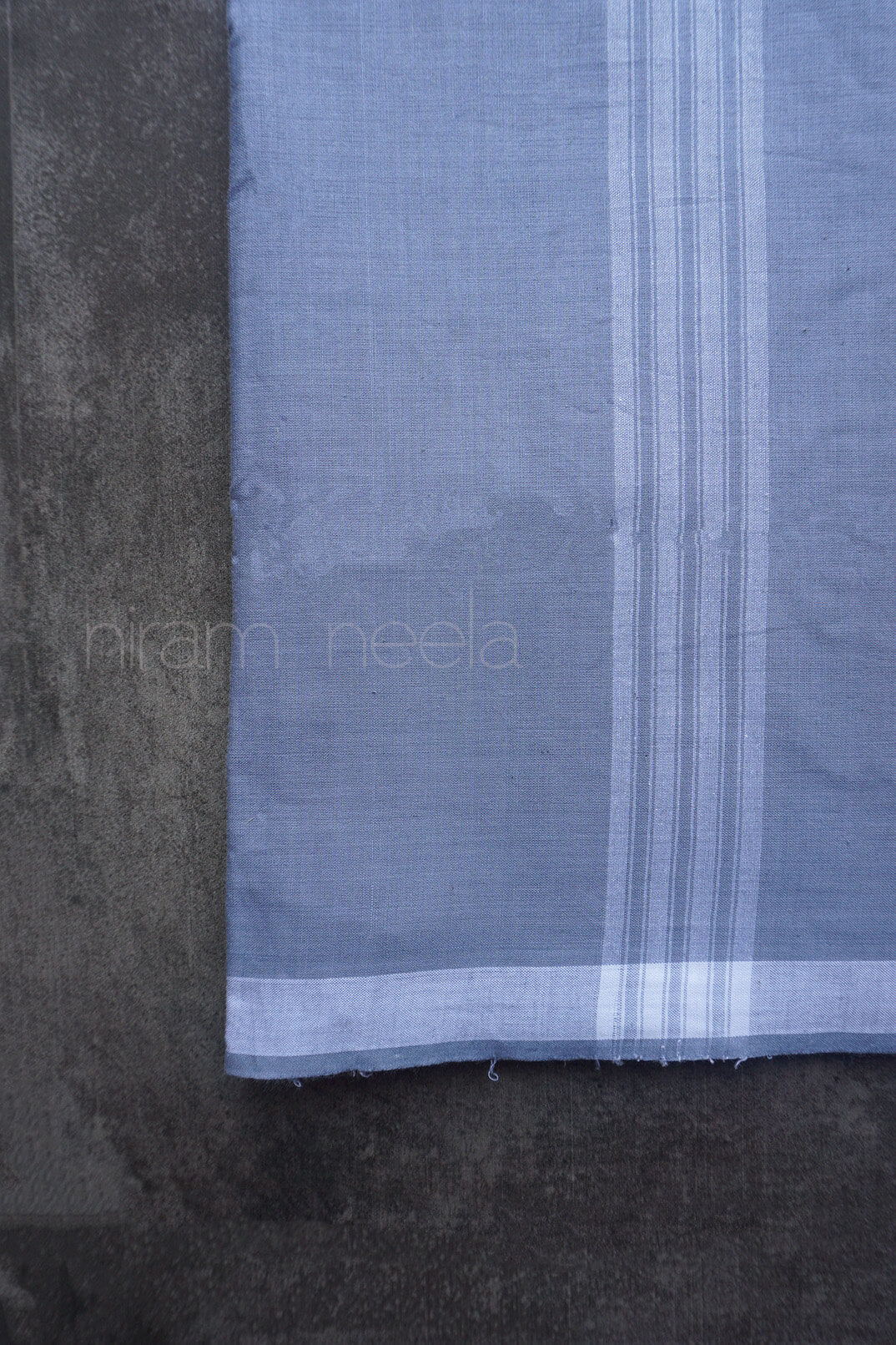 Close-up of a grey dhoti with white stripes on a dark background, featuring the brand 'niram neela'.
