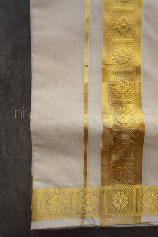 Close-up of a cream dhoti with a gold border featuring floral patterns on a dark background.