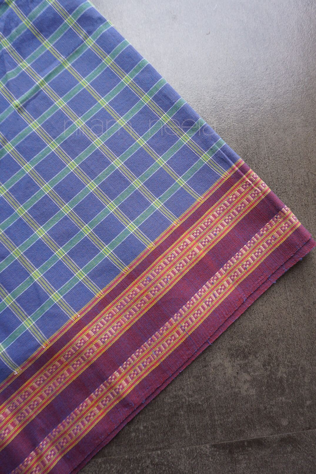 A blue and green checkered fabric with a maroon border against a dark grey background