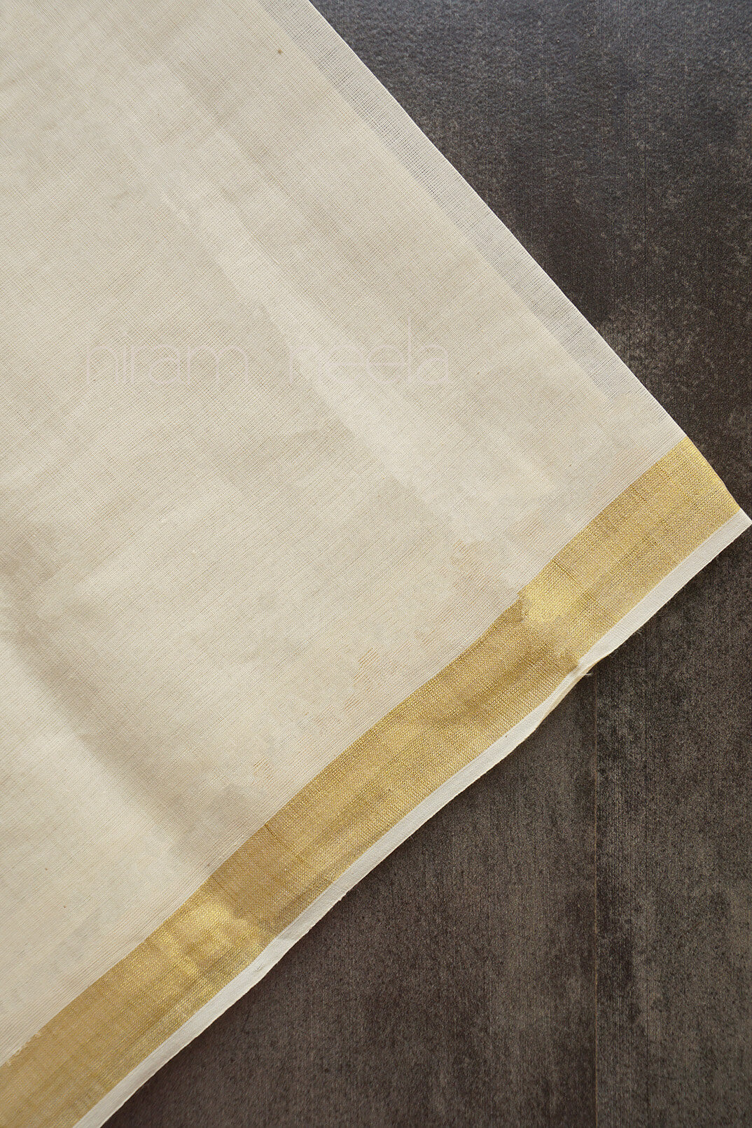 Cream fabric with a gold border on a textured dark surface | Niram Neela