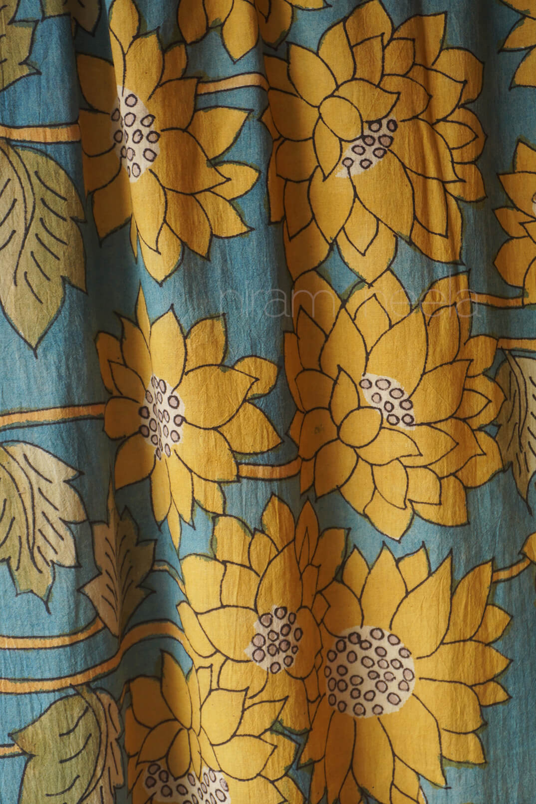 A close-up of a fabric  featuring large mustard yellow lotus flowers and green leaves on a muted teal-blue background.