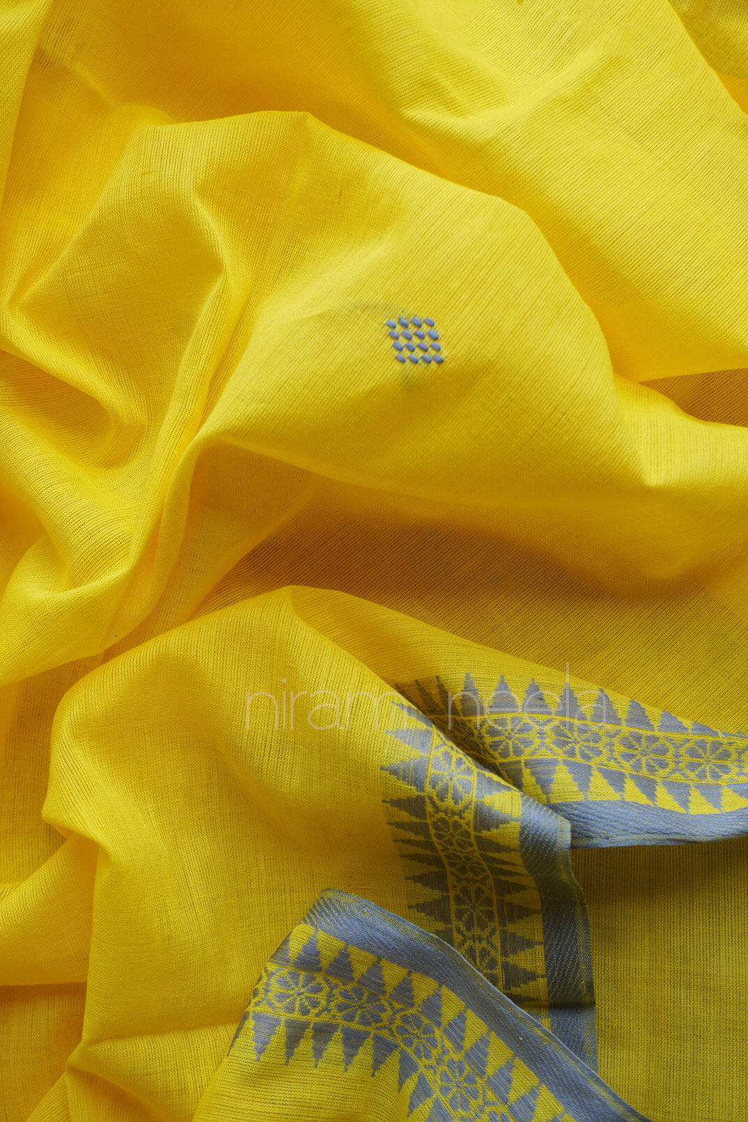 Yellow fabric with a small blue checkered motif and a blue patterned border, shown in a close-up draped view.