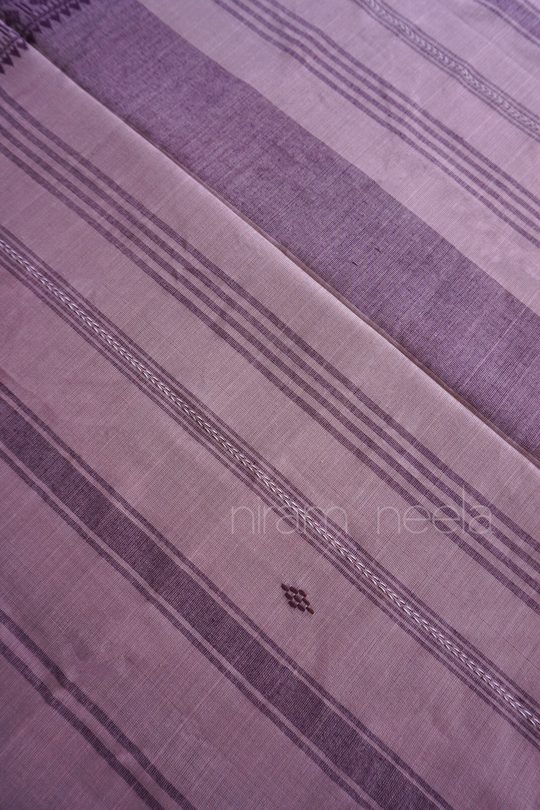 A close-up of a woven textile with a lavender-purple and dusty pink striped pattern, featuring a small woven geometric motif near the center.