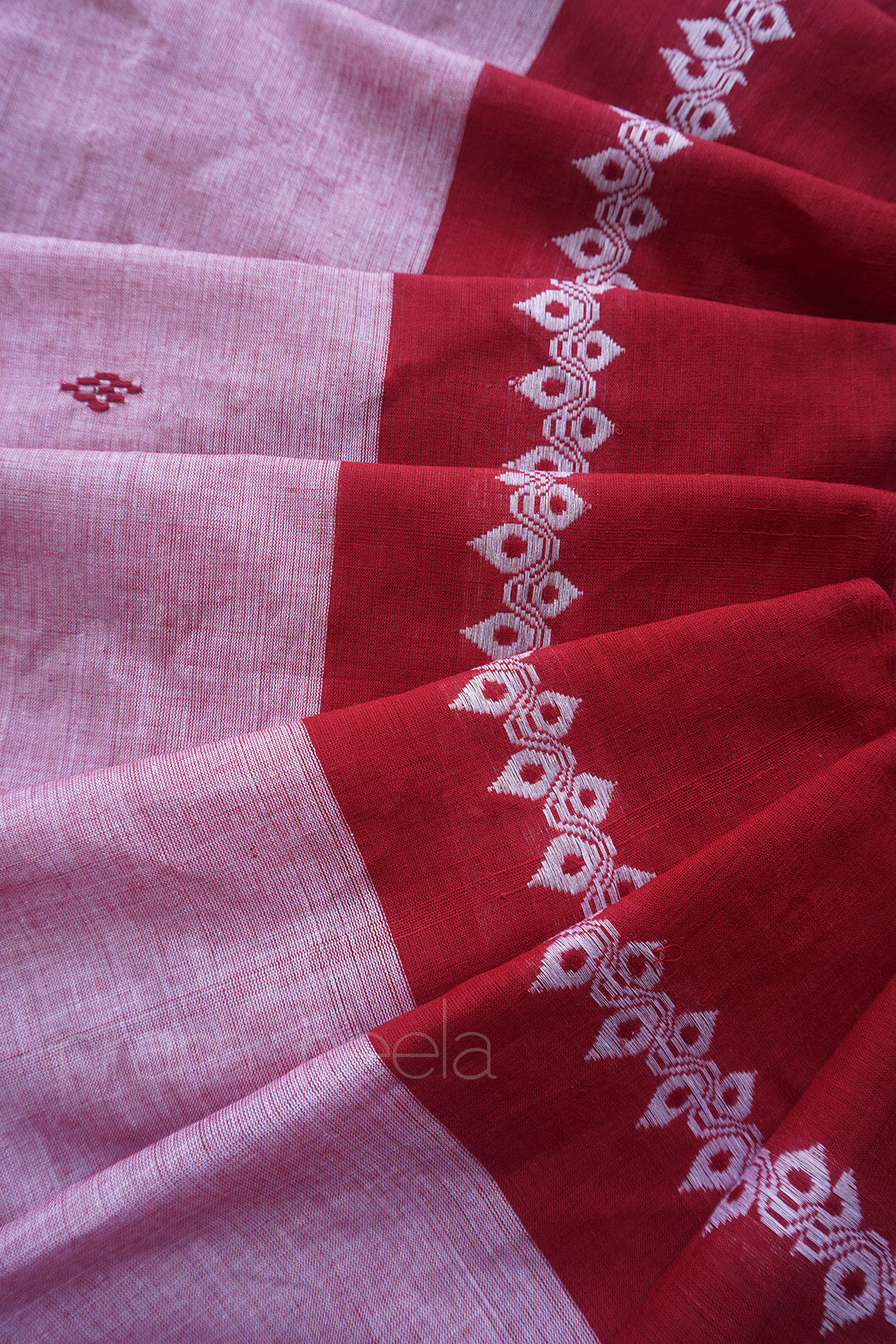A close-up of a draped red and light pink sari, featuring a white woven border with geometric and floral motifs.