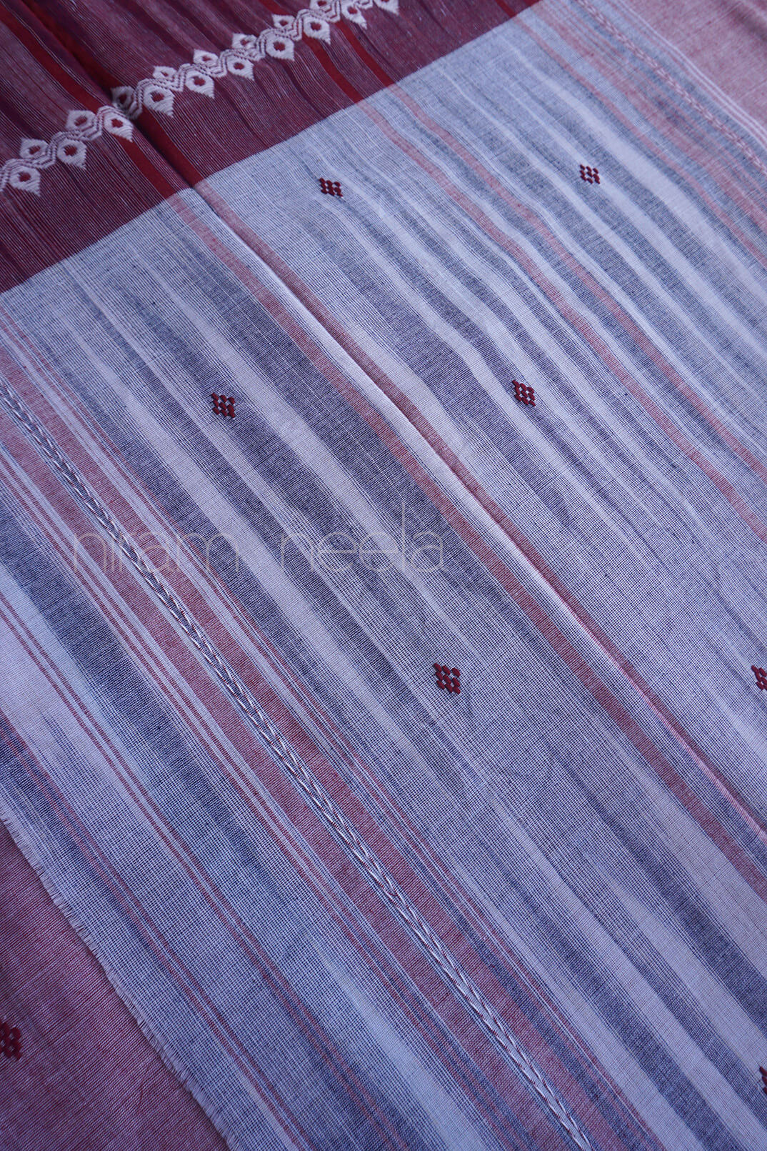 A close-up of a striped pallu of a sari, featuring horizontal bands of dusty purple, gray, and muted red with small woven diamond motifs.