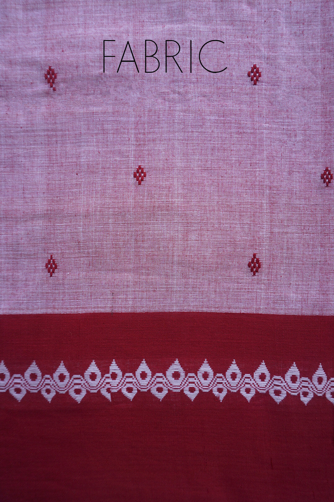 A close-up of a grey saree with a light grey body , a deep red border, and a white decorative border along the bottom. The word 'FABRIC' is printed at the top. 