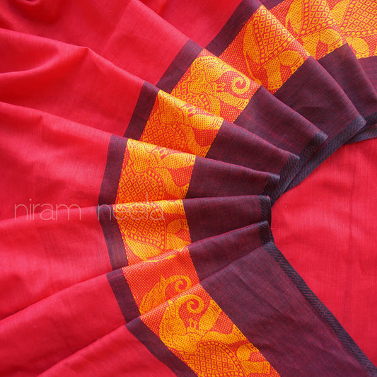 A close-up of a red saree, arranged in a fan pattern to display its border. The border features a wide yellow and orange patterned band with traditional motifs, flanked by black borders.