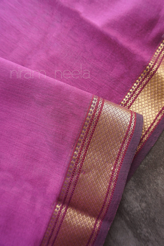 A close-up of a purple silk cotton fabric, featuring a prominent metallic gold border with woven patterns and thin red accent stripes. The brand name 'niram neela' is faintly watermarked on the upper left.