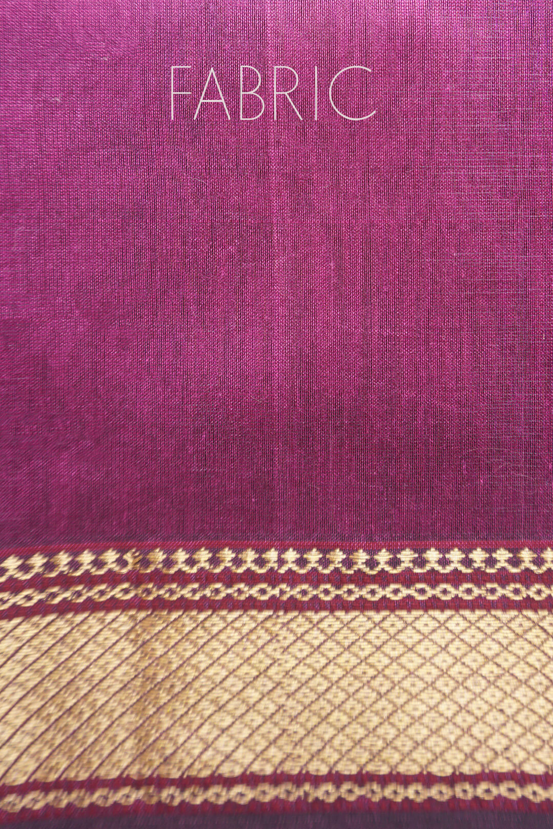 A close-up of a magenta-purple woven fabric with a wide gold zari border and the word 'FABRIC' printed in white at the top.