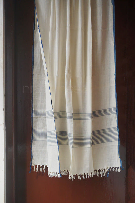 An off-white cotton shawl with thin blue stripes and fringed edges, hanging against a dark brown wooden door.