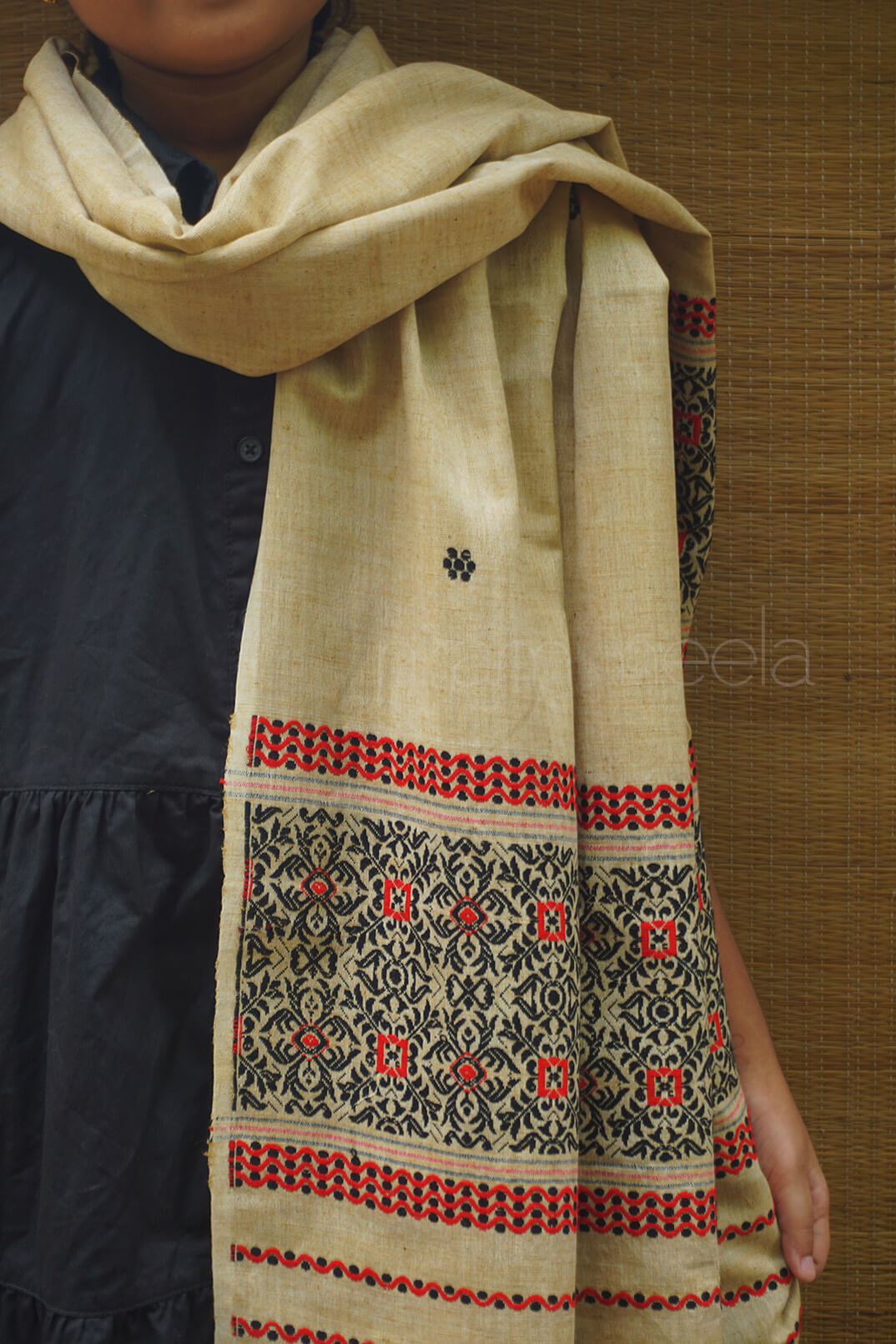 Beige scarf with black and red patterns worn by a person against a wooden background