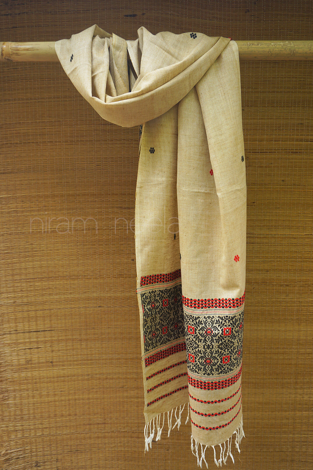 Beige silk scarf with intricate patterns hanging on a wooden rod against a woven background