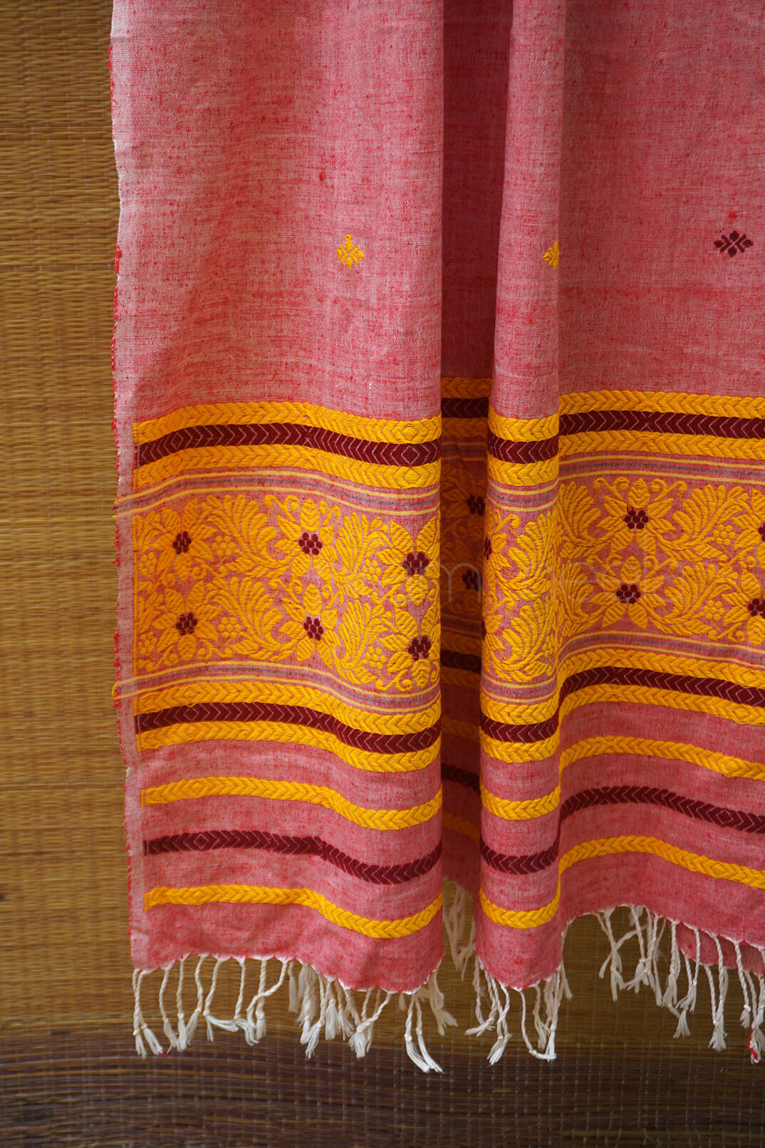 Pink and yellow patterned stole with fringes on a wooden surface