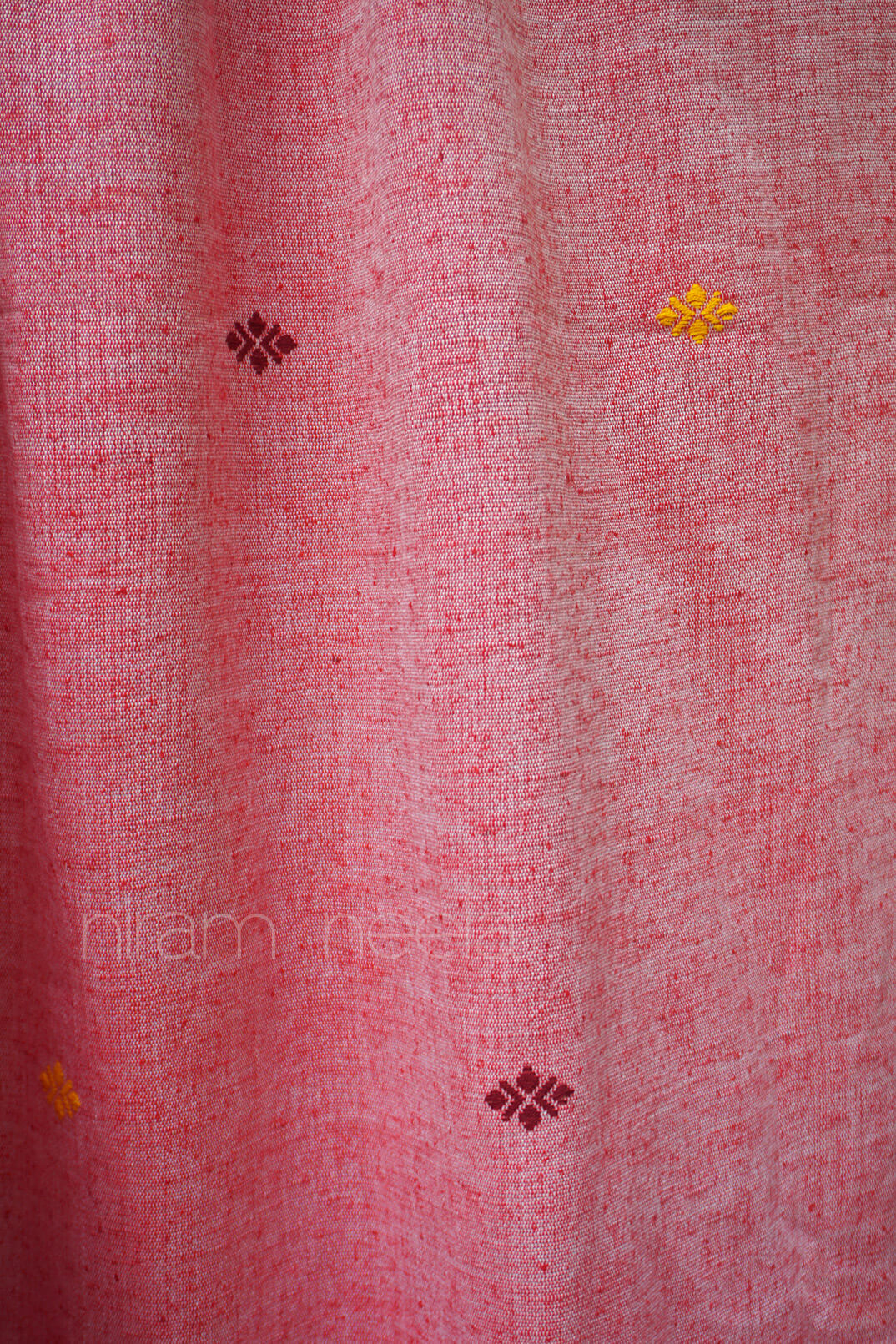 Close-up of a pink fabric with embroidered patterns, brand 'niram neela' visible.