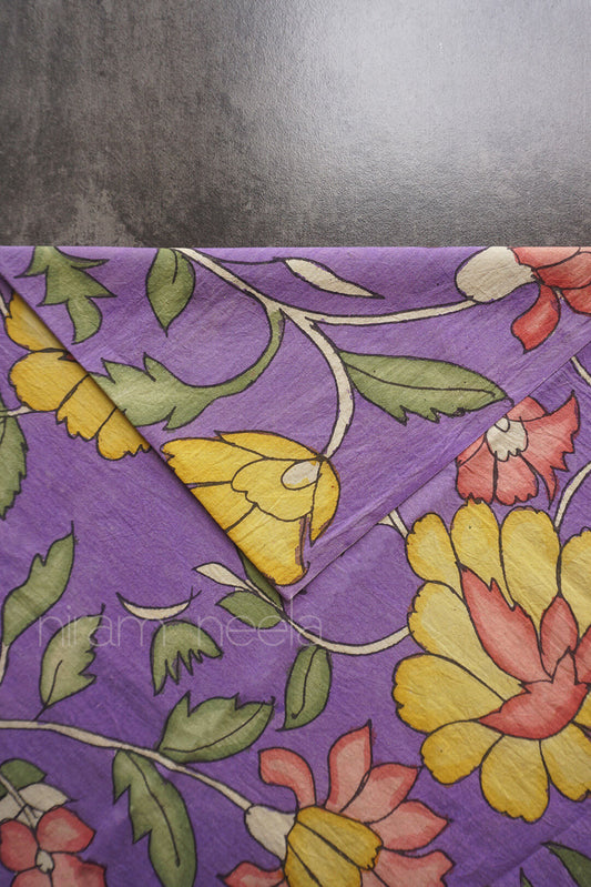 A close-up of a violet fabric with a vintage floral pattern featuring yellow, pink, and green flowers and leaves, folded over on a dark gray surface.
