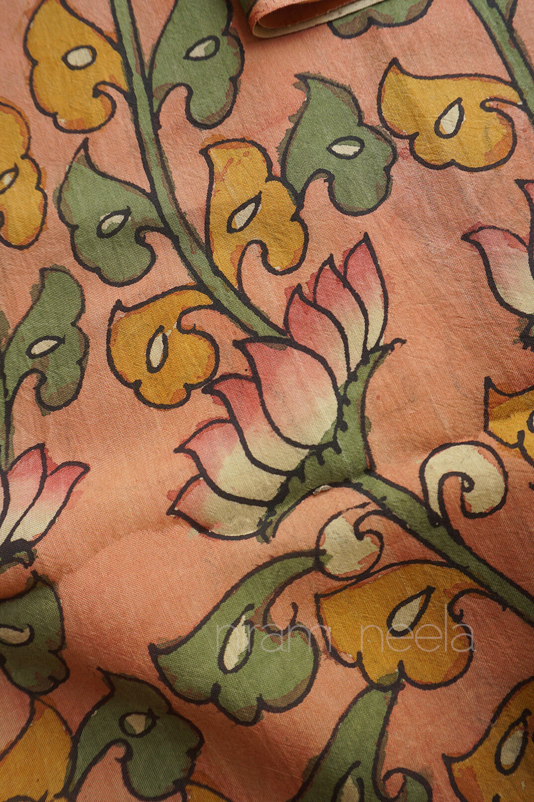 A close-up of a peach-colored fabric with a hand-painted floral pattern in yellow, green, and pink, featuring a visible 'niram neela' watermark.