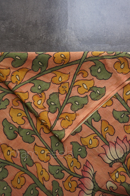 A close-up of a peach-colored fabric with a hand-painted floral design in green and mustard yellow, featuring a lotus flower motif.