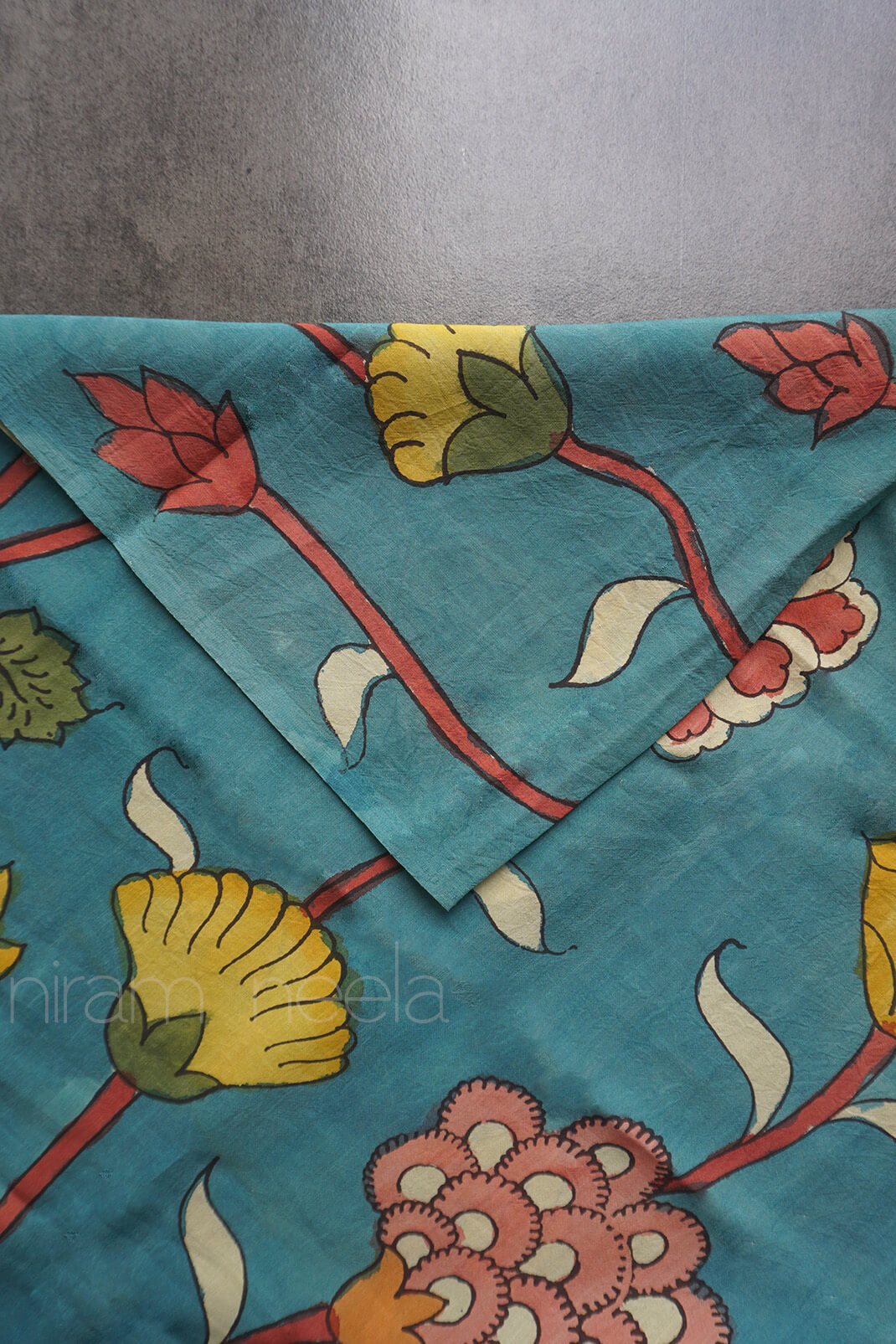 Blue floral silk Kalamkari fabric with yellow and red floral design details displayed against a grey background