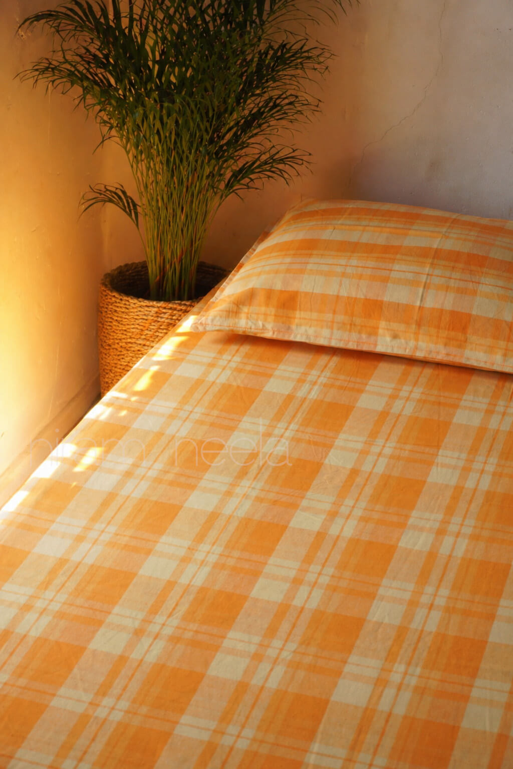 Bed with orange checkered bedding and a plant in the corner.