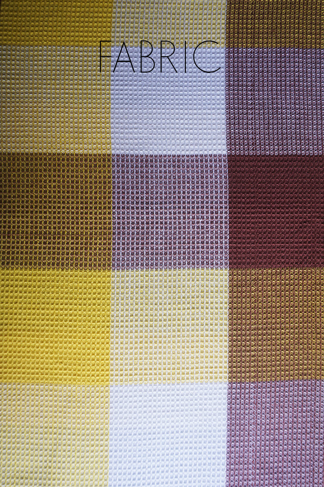 A close-up of a woven fabric swatch with a plaid pattern in mustard yellow, white, brown, and mauve, with the word 'FABRIC' overlaid at the top.