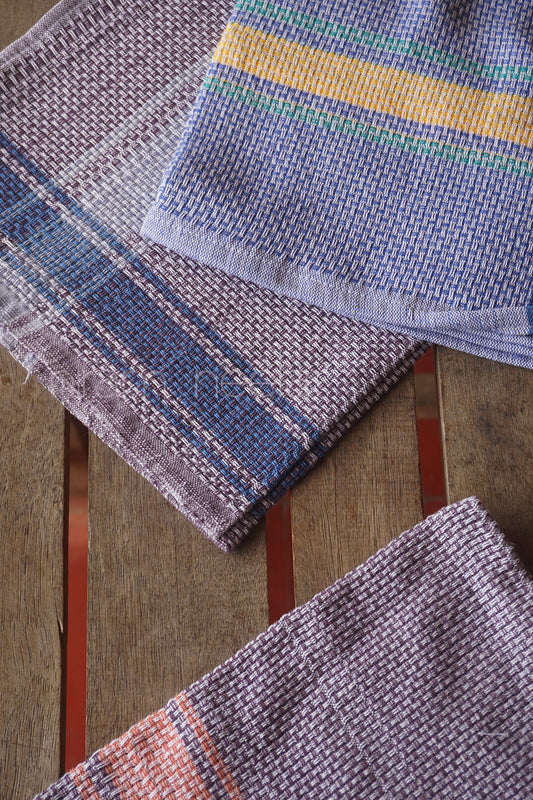 Three woven kitchen towels of different colors on a wooden surface