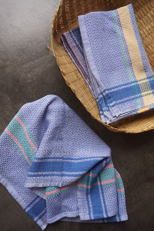 Three woven kitchen towels of different colors on a dark surface | Home linen by Niram Neela