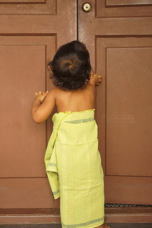 Child wrapped in a green towel standing in front of a wooden door | Bed and bath by Niram Neela