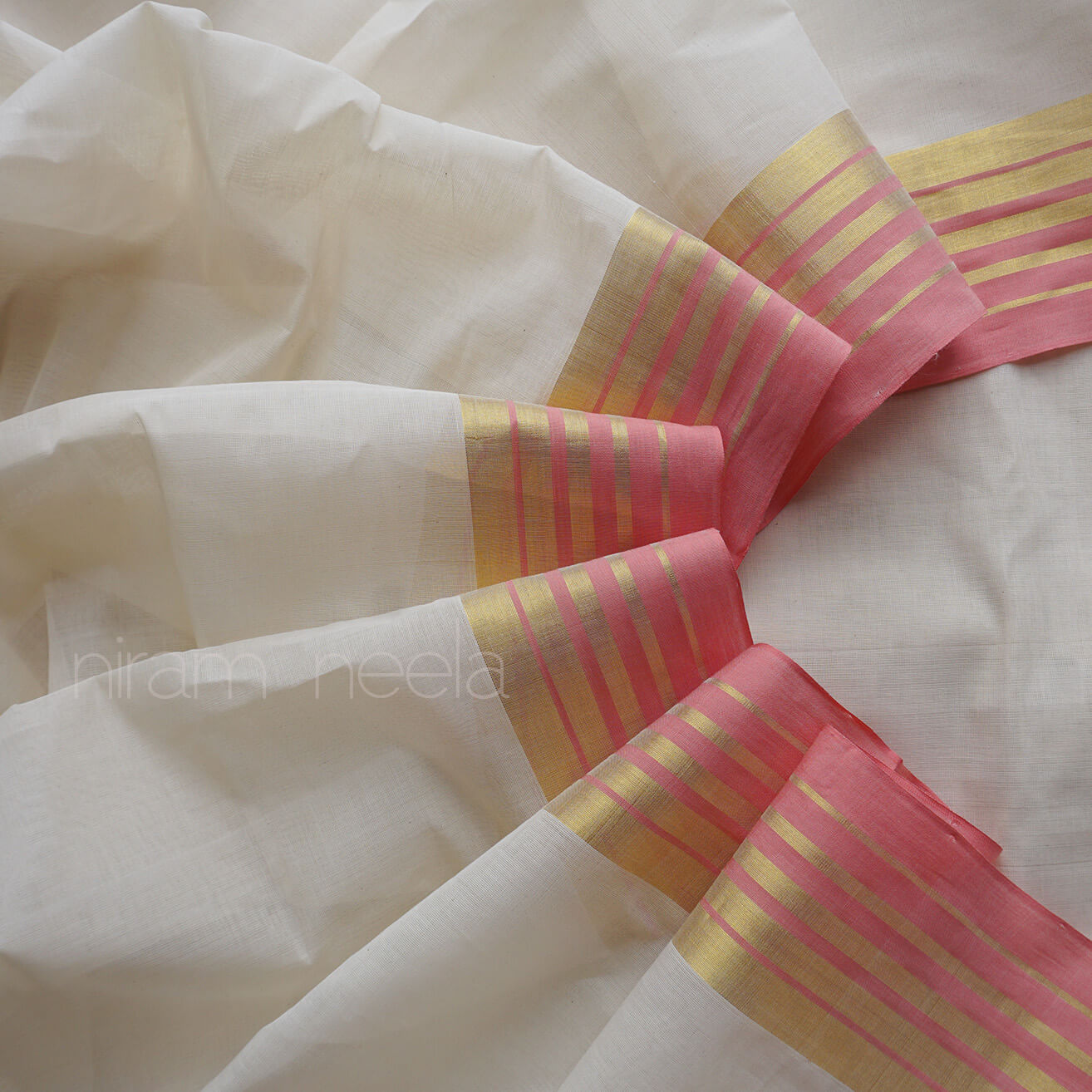 White fabric with pink and gold striped borders, brand 'nilam neela' visible.
