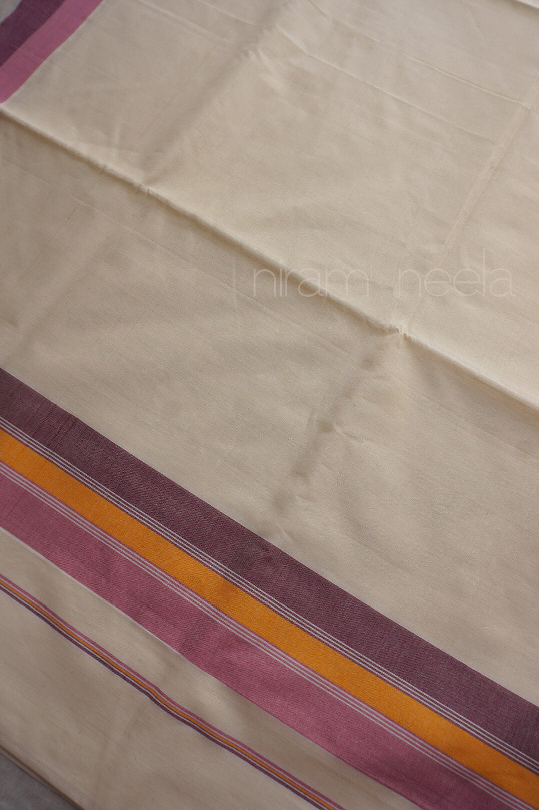 A close-up of a cream-colored saree, featuring a decorative border with stripes of purple, orange, and pink.