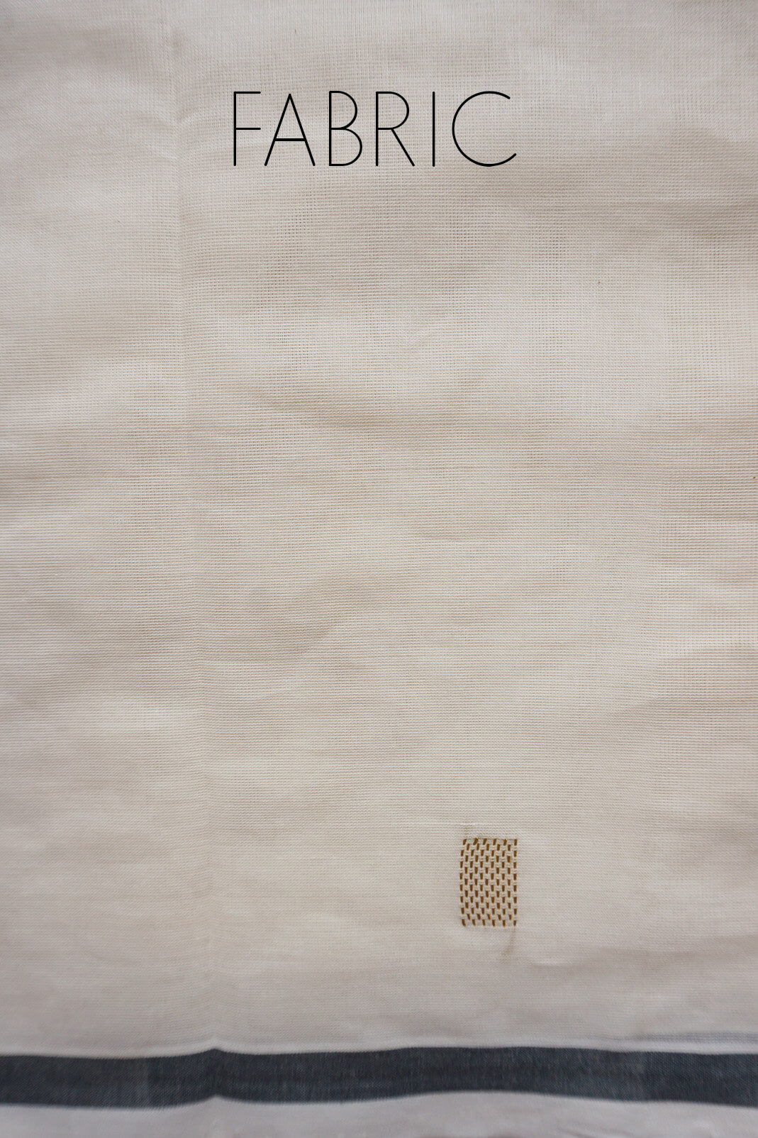 A close-up of an offwhite saree with the word 'FABRIC' printed at the top and a small woven sample patch near the bottom right.
