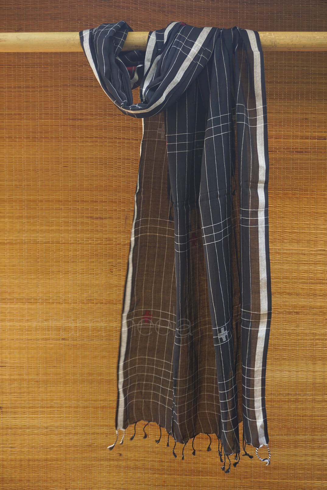 Black cotton scarf with red and white pattern draped over a wooden rod against a woven background.