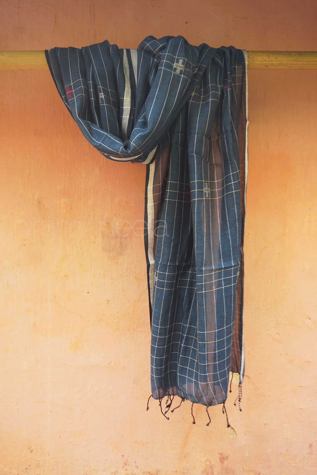 Blue plaid scarf hanging on a wooden rod against a beige wall.