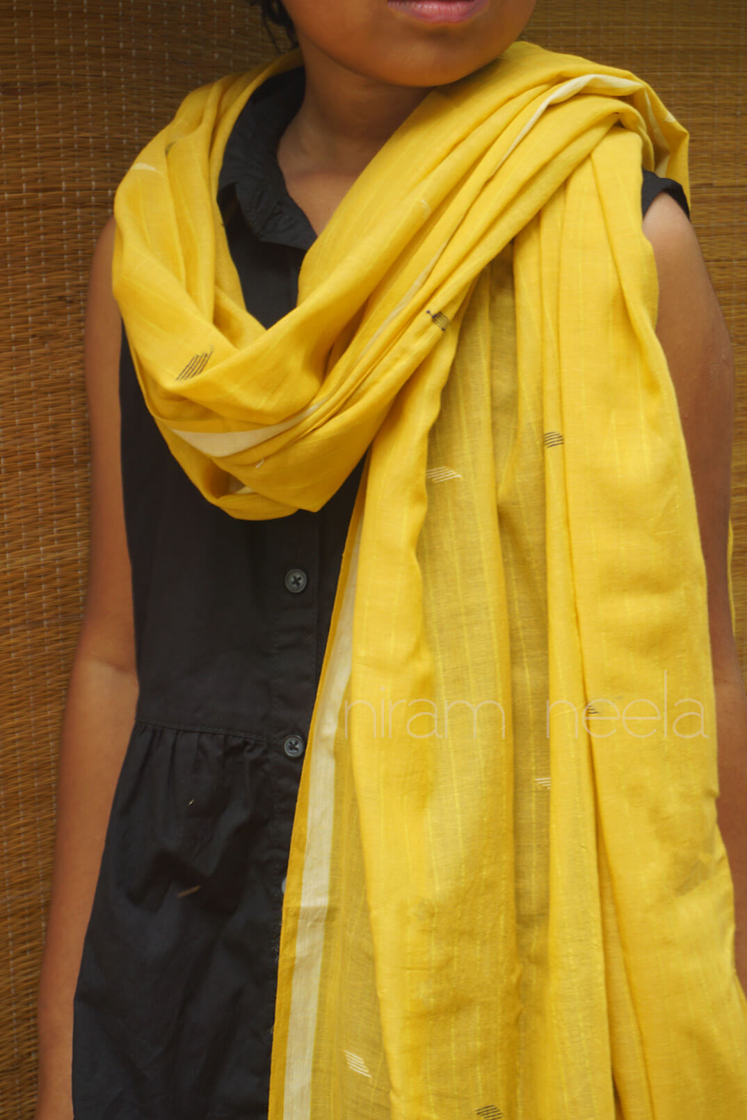 Person wearing a yellow scarf over a black top against a brown background