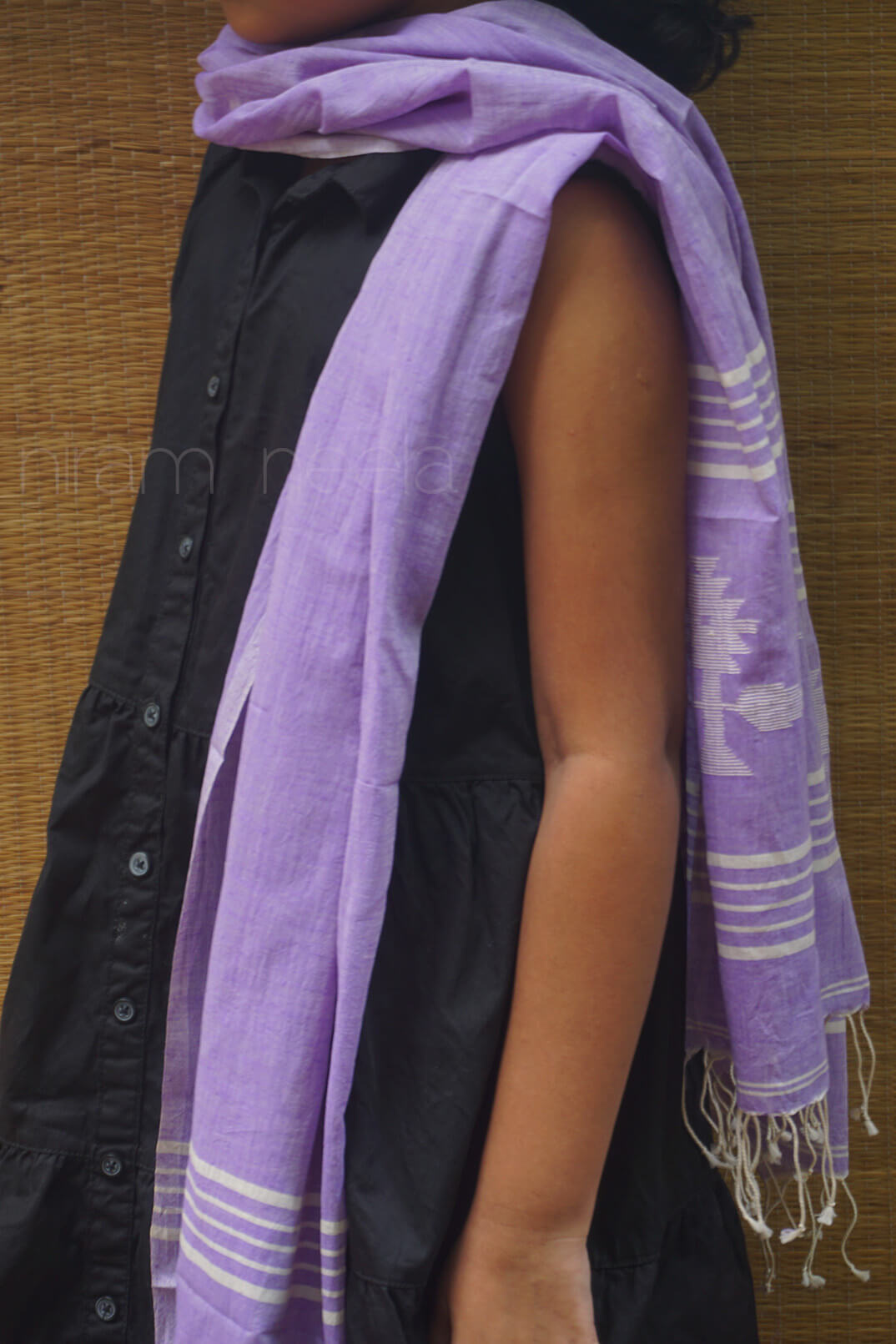 Person wearing a soft violet scarf with white patterns over a black shirt against a wooden background