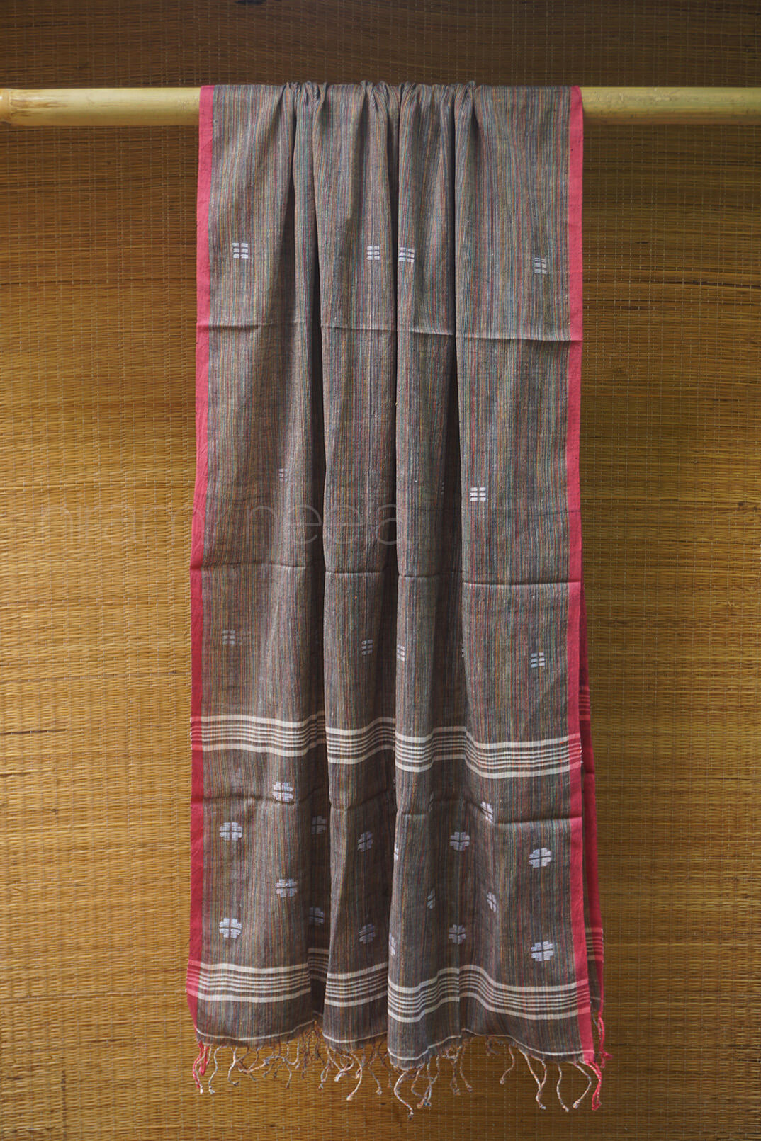 Brown fabric with red border and white patterns draped over a wooden rod on a wooden background