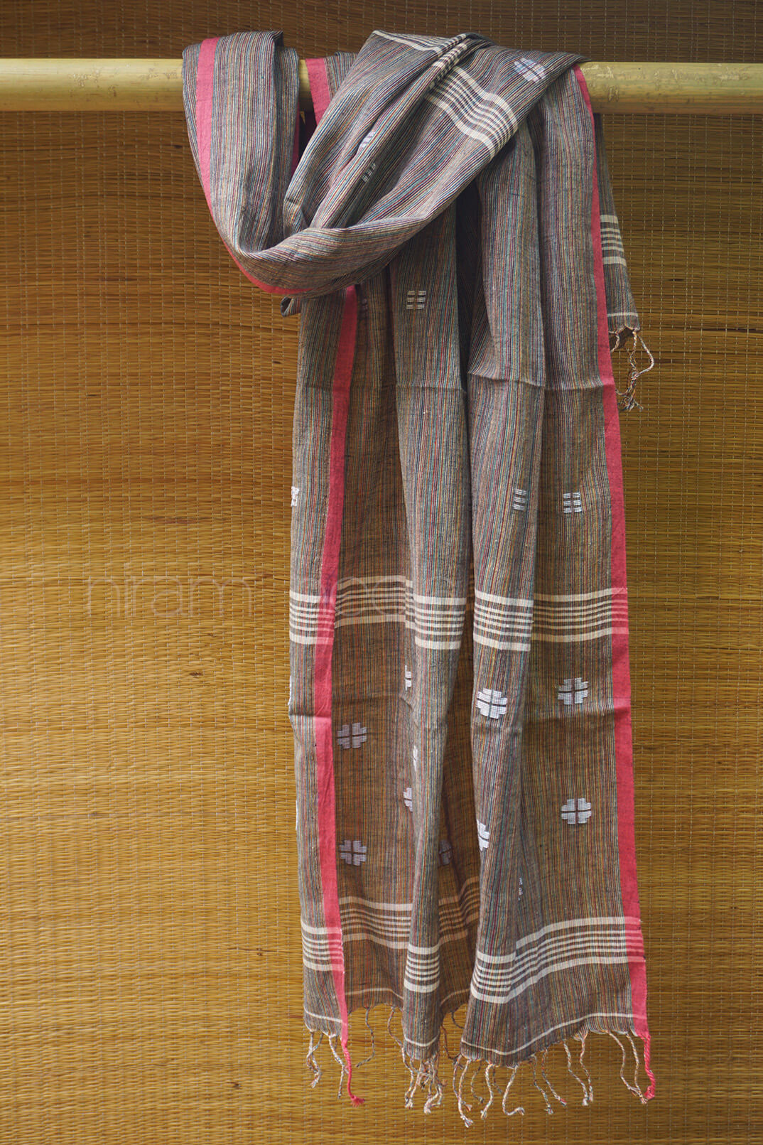 Textured scarf with red and gray patterns draped over a bamboo rod against a woven background