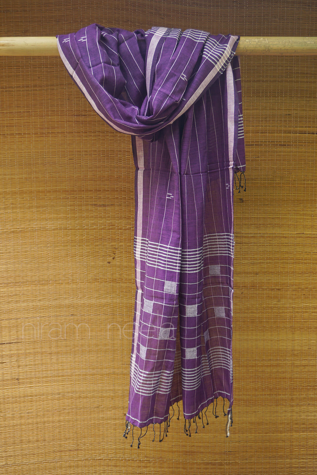 Purple and white checkered scarf with tassels on a wooden rod against a woven bamboo background