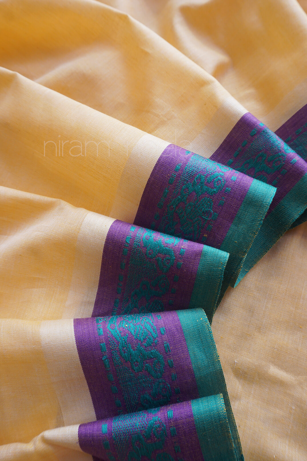 Close-up of a cream saree with purple and green border , brand 'niram neela' visible