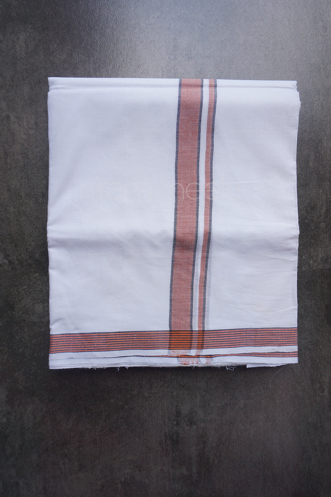 A folded white dhoti, featuring a vertical stripe pattern in rust orange, white, and thin dark lines, with a matching horizontal stripe border at the bottom, laid flat on a dark textured surface.