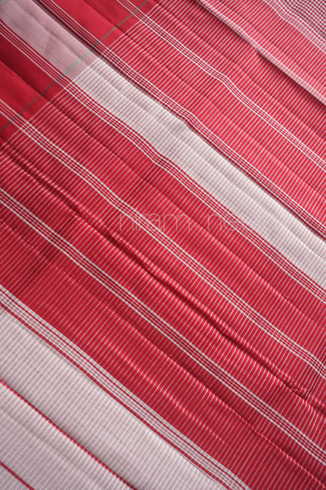 A close-up of a red and white striped fabric with fine woven texture and diagonal folds.