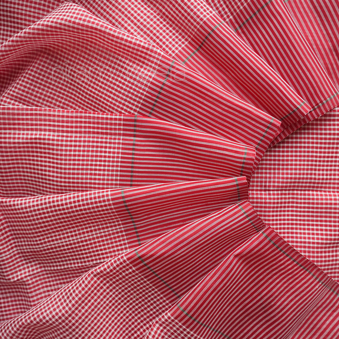 A close-up of saree with a red and white gingham pattern and thin green diagonal stripes, arranged in soft folds.
