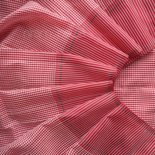 A close-up of saree with a red and white gingham pattern and thin green diagonal stripes, arranged in soft folds.