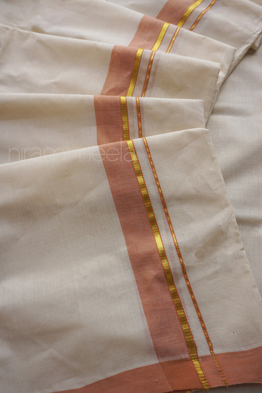 A close-up of a folded off-white Kerala dhoti with a vertical peach border and narrow metallic gold stripes, laid out on a matching fabric background.