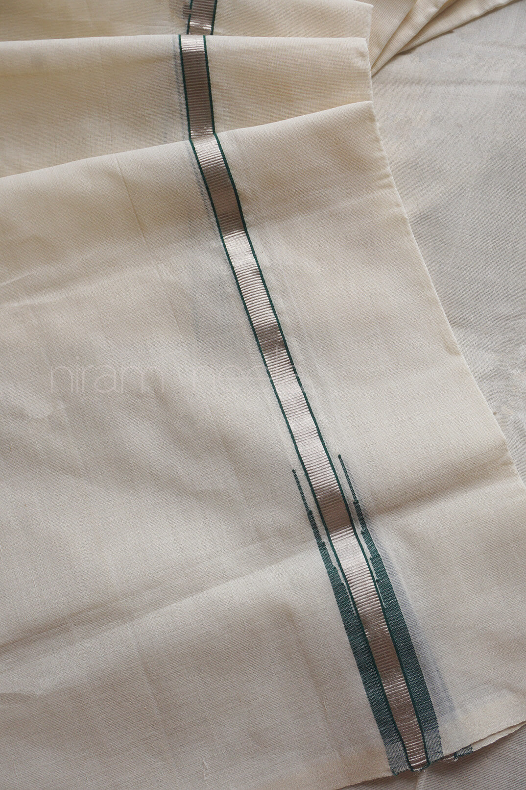 A close-up of a light cream-colored dhoti, featuring a central vertical green and silver stripe flanked by thin dark green borders.