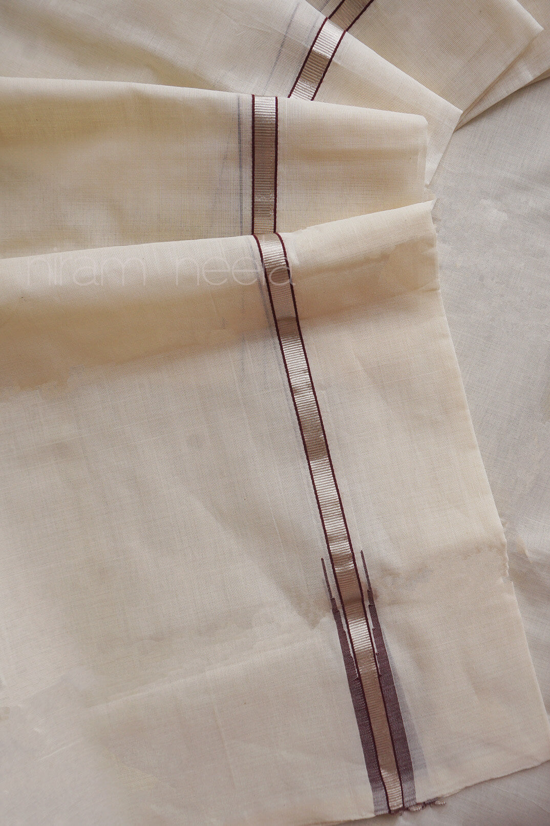 A close-up of a cream-colored dhoti,  featuring a central vertical border with metallic silver stripes and thin brown accent lines.