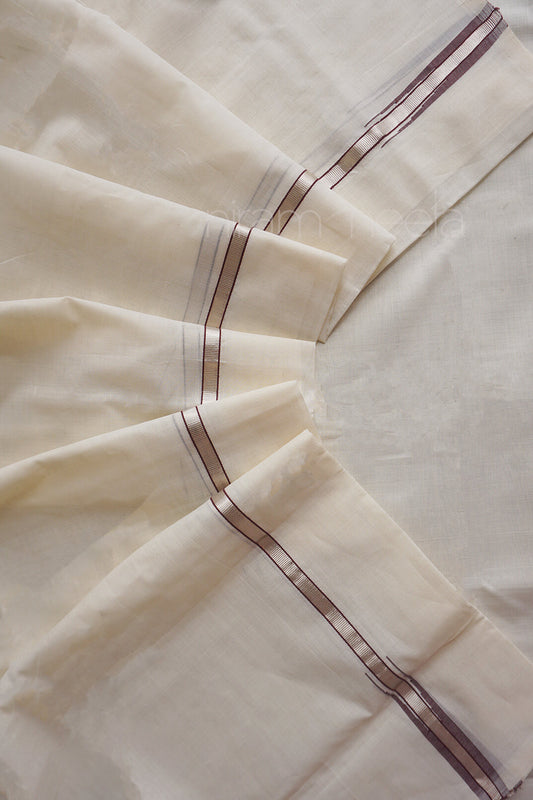 A close-up of cream-colored mundu with a subtle woven texture and thin brown  and silver stripes running along the folded edges.